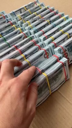 a person is holding money in front of a pile of hundred dollar bills on a table