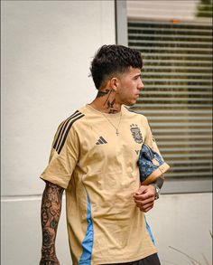 a man with tattoos standing in front of a building wearing a yellow shirt and black shorts