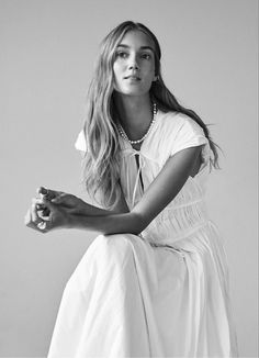 a woman sitting on top of a chair wearing a white dress and pearl necklaces