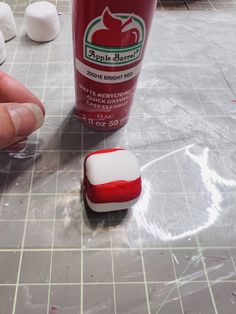 a hand is pointing at a red and white toothpaste on the ground next to a cup