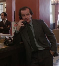 a man in a suit is talking on the phone while another man stands behind him