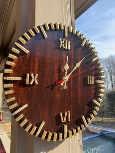 a large wooden clock with roman numerals on the side of a building next to a swimming pool