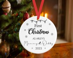 personalized first christmas ornament hanging from a christmas tree with lights in the background