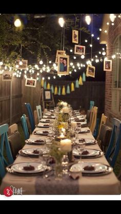 a long table is set with place settings and pictures hanging from the ceiling above it