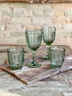 four green glass goblets sitting on a wooden tray next to a brick wall