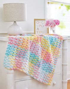 a crocheted blanket sitting on top of a white dresser next to a lamp