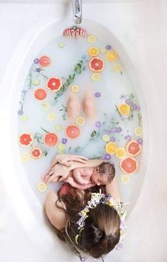 a woman laying in a bathtub with flowers and fruit on the tub side as she holds her baby