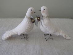 two white birds standing next to each other on top of a bed covered in linen