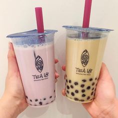 two people holding up drinks with straws in their hands on a white wall background