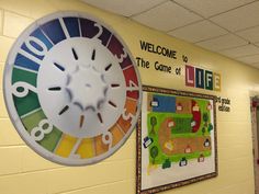 a large clock hanging from the side of a wall in front of a welcome to the game of life sign