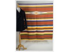 an orange, yellow and blue striped blanket hanging on a wall next to a coat rack