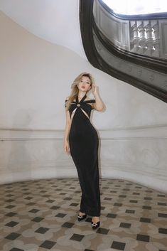 a woman in a black dress standing on a tiled floor and posing for the camera