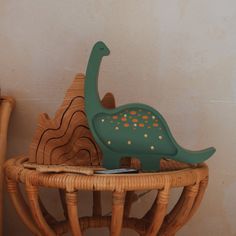 a green dinosaur toy sitting on top of a wicker chair next to a wall