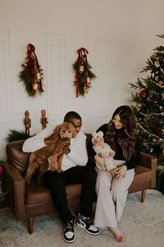 a man and woman sitting on a couch with a baby in front of a christmas tree