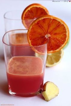 two glasses filled with juice next to sliced oranges