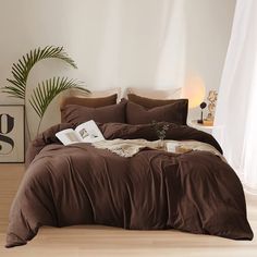 a bed with brown sheets and pillows in a white room next to a potted plant