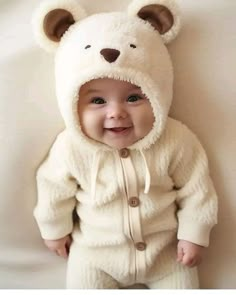 a baby wearing a white bear suit and smiling