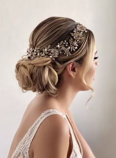 a woman wearing a bridal headpiece with flowers on it's side and her hair in a low bun