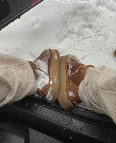 someones feet in the snow with some food on their car door handle and gloved hands