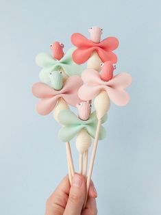 a hand holding four small candy lollipops in pastel colors