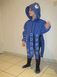 a young boy in a blue costume standing next to a white wall and tiled floor