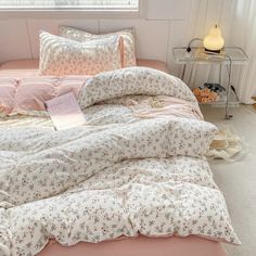 a bed with pink comforter and pillows in a white room next to a window