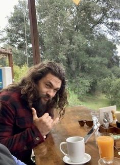 a man with long hair and beard sitting at a table in front of an orange juice