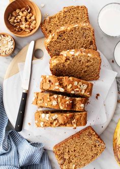 sliced loaf of banana nut bread on a plate next to two glasses of milk and bananas