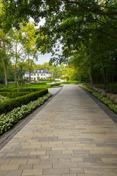 an empty walkway in front of a large white house surrounded by trees and bushes on both sides