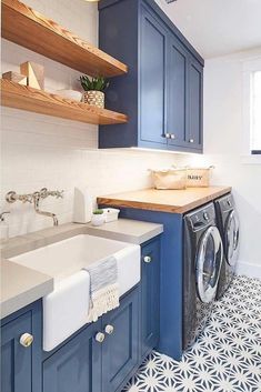 a washer and dryer in a small room with blue cabinets, white tile flooring and wooden shelves