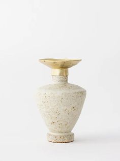 a white and gold vase sitting on top of a table next to a white wall