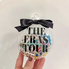 a hand holding up a glass ornament with the words eras tour on it