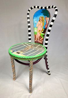 a painted chair sitting on top of a white floor next to a table with a painting on it