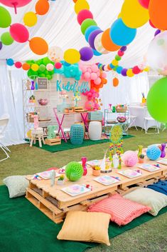 an outdoor party with balloons, plates and napkins on the grass under a tent