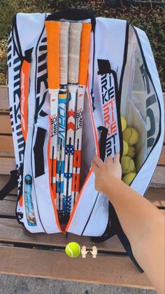 a tennis racket and ball in a bag on a bench with someone's hand reaching for it