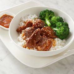 a white plate topped with rice and meat next to broccoli covered in sauce