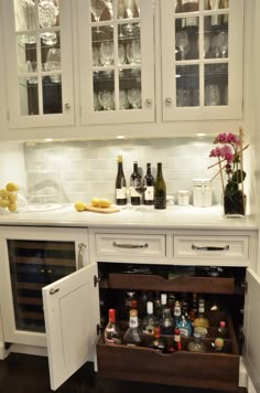 an open cabinet in the corner of a kitchen with wine glasses and bottles on it