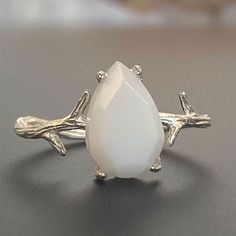 "For fans of minimalist nature-inspired jewelry, we created our stand-out Mother Nature Silver breastmilk ring. It pairs together a branch-like sterling silver ring band with an exquisite yet small pear-shaped faceted breastmilk stone. Go with your natural breast milk or combine your breast milk with opal effect flakes or pearl powder. Opalizing your breast milk adds a pale, milky opal appearance to your breastmilk stone that catches the light and reflects pastel rainbow hues, while adding pearl Delicate White Moonstone Ring In Sterling Silver, Delicate White Moonstone Gemstone Ring, Delicate White Moonstone Ring, Minimalist White Moonstone Ring In Sterling Silver, White Teardrop Sterling Silver Rings, Adjustable White Moonstone Ring As Gift, White Sterling Silver Nature-inspired Jewelry, Minimalist Handmade White Moonstone Ring, White Adjustable Moonstone Ring As Gift