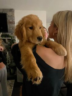 a woman holding a dog in her arms while other people watch from the back ground