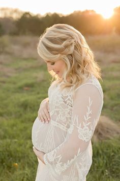 a pregnant woman standing in the grass at sunset