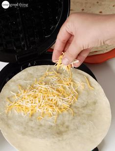 a person scooping cheese from a tortilla shell into a waffle maker