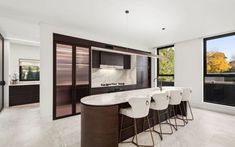 a kitchen with marble counter tops and bar stools in front of large open windows