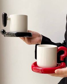 a person holding two coffee mugs in their hands, one is red and the other is white