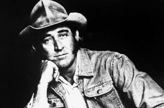 a black and white photo of a man wearing a cowboy hat with his hand on his chin