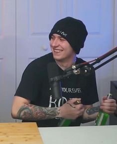 a man sitting at a table with a microphone in front of him and wearing a black hat