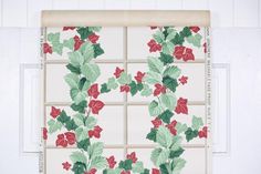 a window with red and green flowers on it's side, behind which is a roller shade