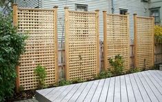 a wooden deck in front of a house with a trellis on the fence and bushes growing next to it