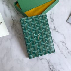 a green and gold patterned wallet sitting on top of a marble counter next to a card case