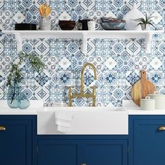 a kitchen with blue and white tiles on the backsplash, gold faucet, brass faucet, wooden cutting board