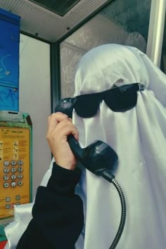 a person in a ghost costume is talking on the phone while wearing sunglasses and a headscarf